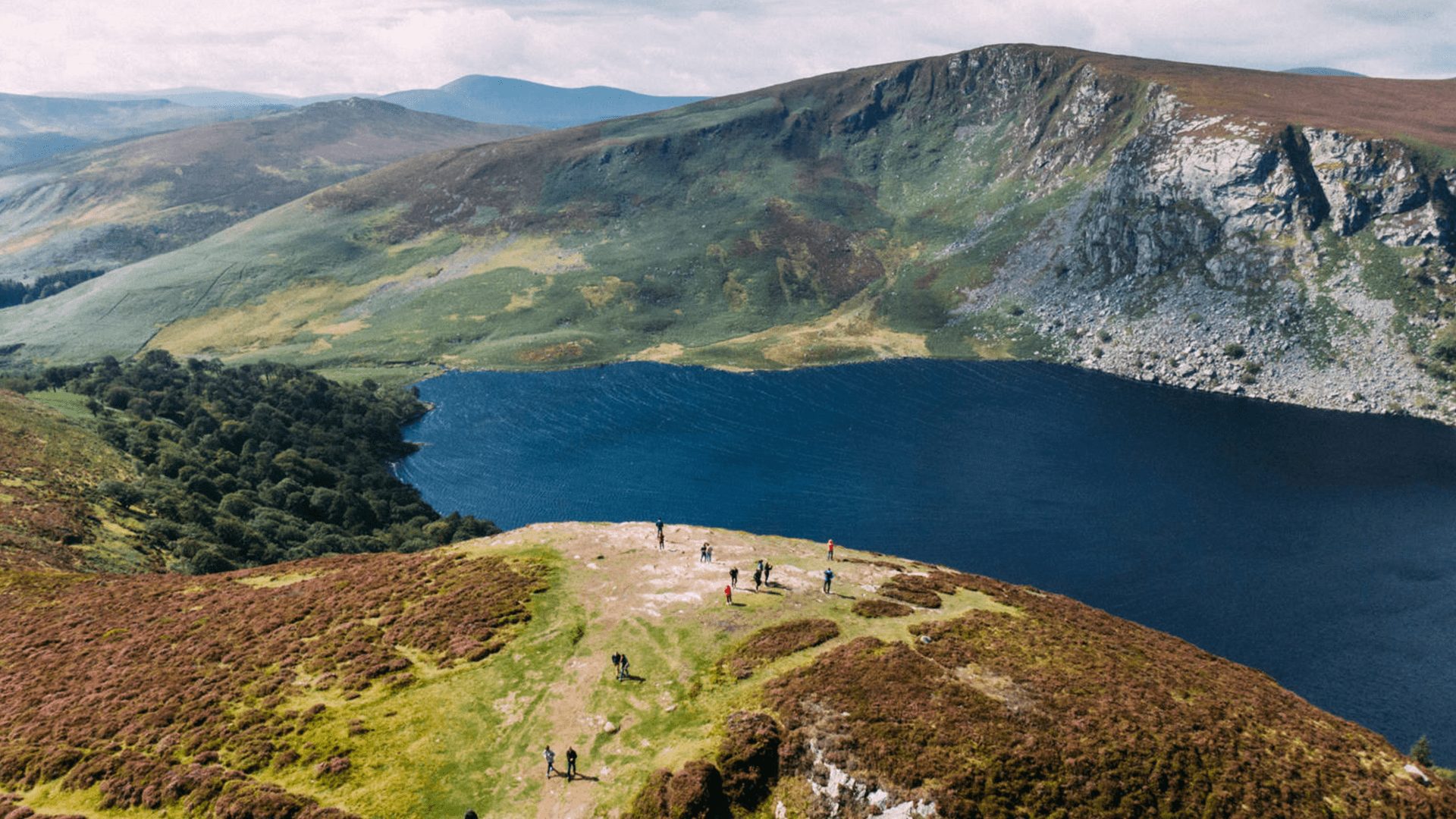 Aerial view of a tour group at the top of the mountain overseeing Lough Tay, Ireland.