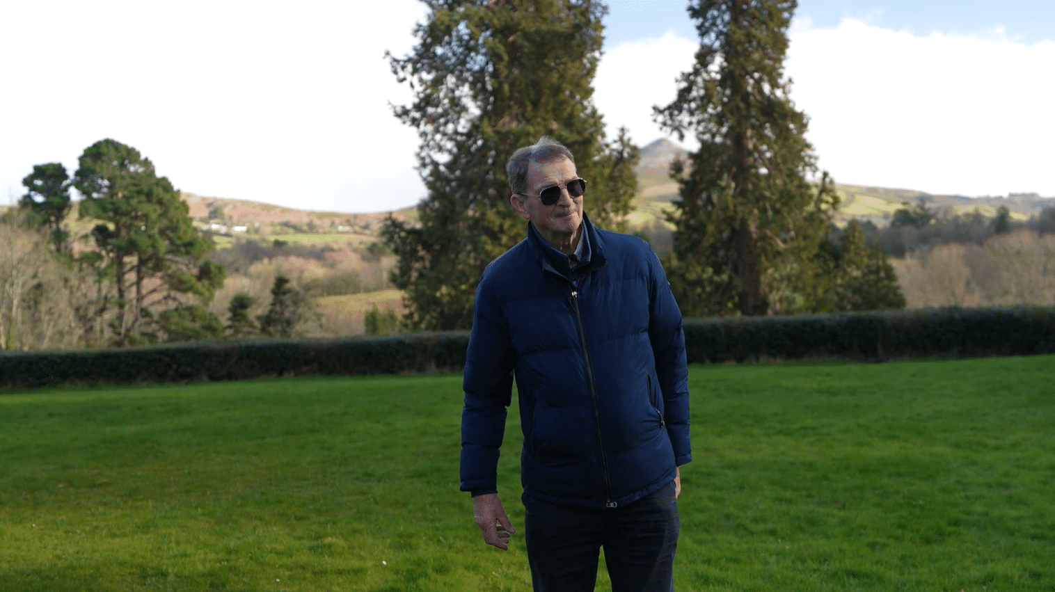 John Ducie, licensed Irish tour guide and horticulturist, standing in lush grounds with mountain scenery on a private tour of Ireland
