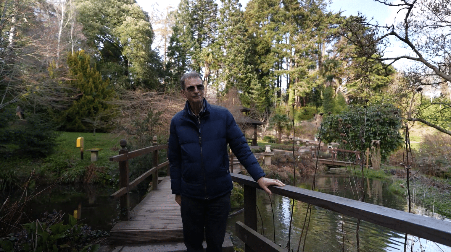 John Ducie, private Irish garden tour guide, standing on a wooden bridge in a scenic woodland garden on a guided tour of Ireland