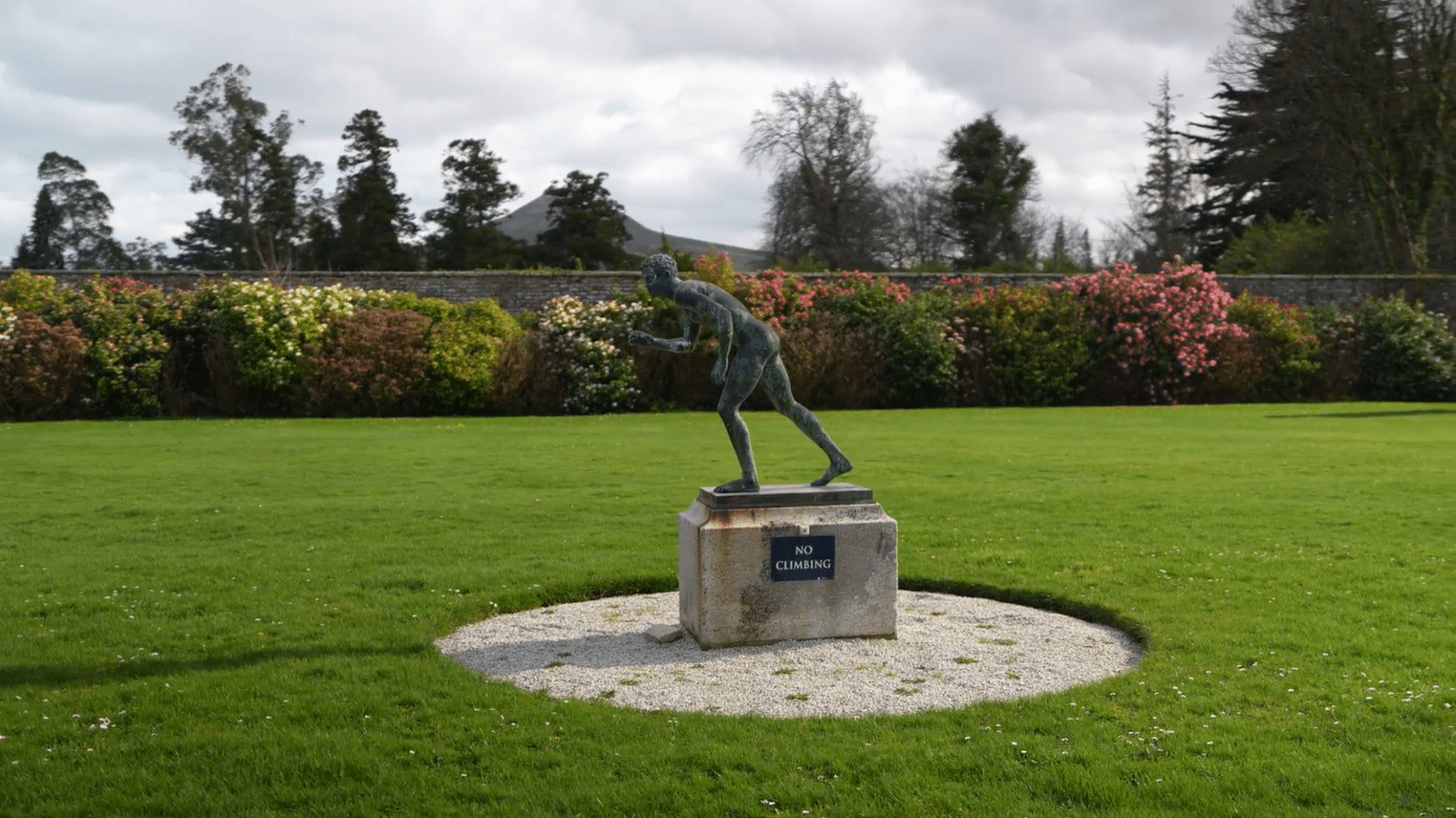 Bronze running figure sculpture in the walled rose garden at Powerscourt Estate, County Wicklow, Ireland, with colourful roses and the Great Sugar Loaf in the background