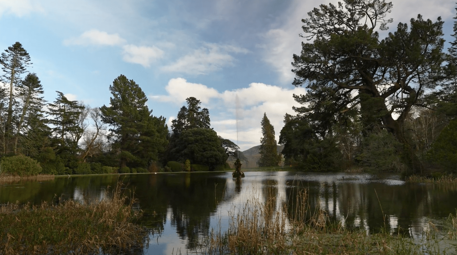 Tranquil view of the lake and Triton fountain at Powerscourt Gardens, Enniskerry, County Wicklow, Ireland, surrounded by ancient trees and rolling Wicklow Mountains