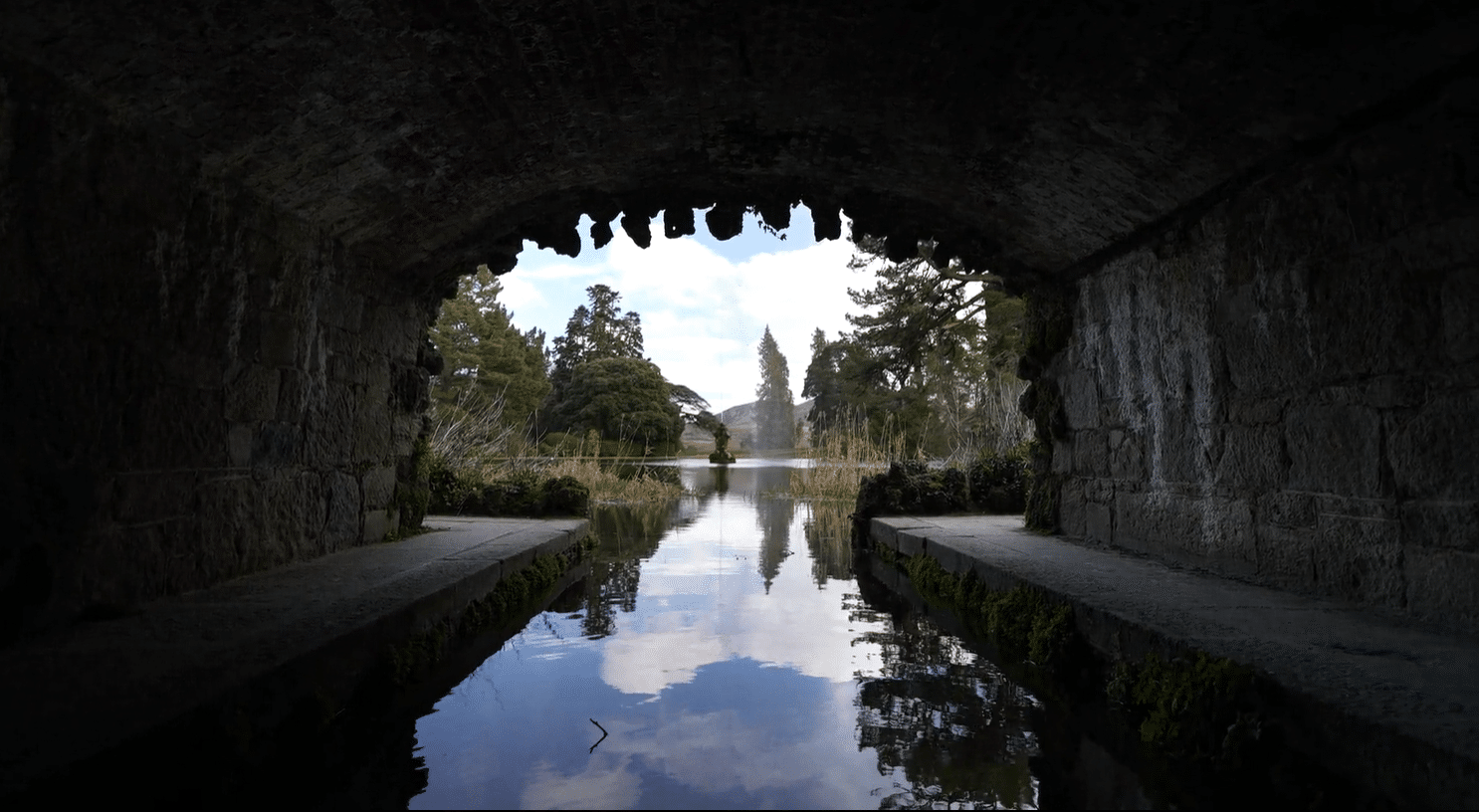 View of the Powerscourt Gardens lake and Triton fountain framed through the stone arch of the bridge tunnel, County Wicklow, Ireland, a highlight of private tours from Dublin